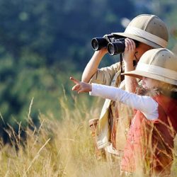 Children brother and sister playing outdoors pretending to be on safari and having fun together with binoculars and hats